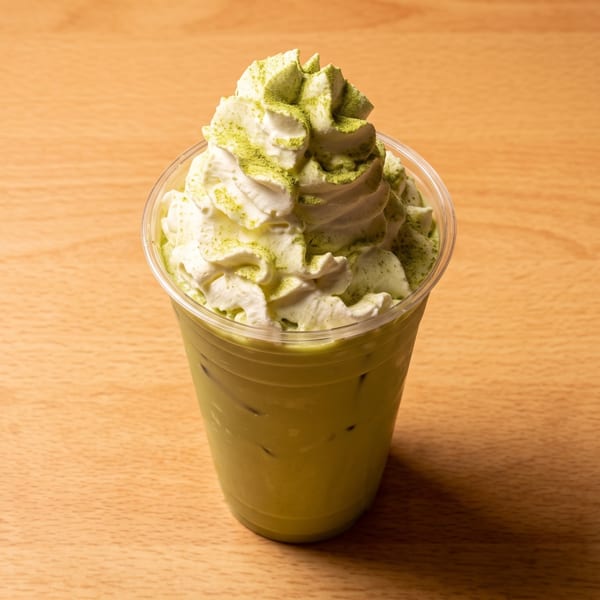 Iced matcha latte with whipped cream and green powder on a wooden table.