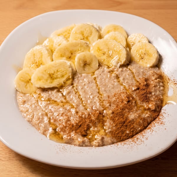 Creamy oatmeal topped with sliced bananas, honey, and cinnamon on a white plate.