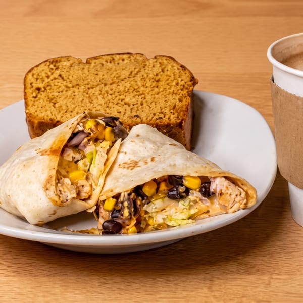 Plate of two stuffed burritos with rice, beans, corn, and cheese, served with toasted bread and coffee.